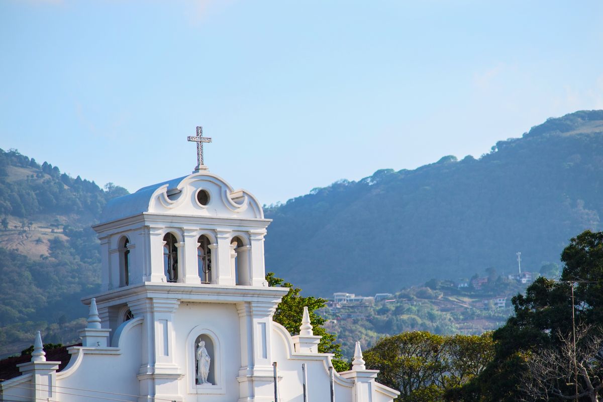The white bell tower of a church in Escazú, with the green hills above the town behind it