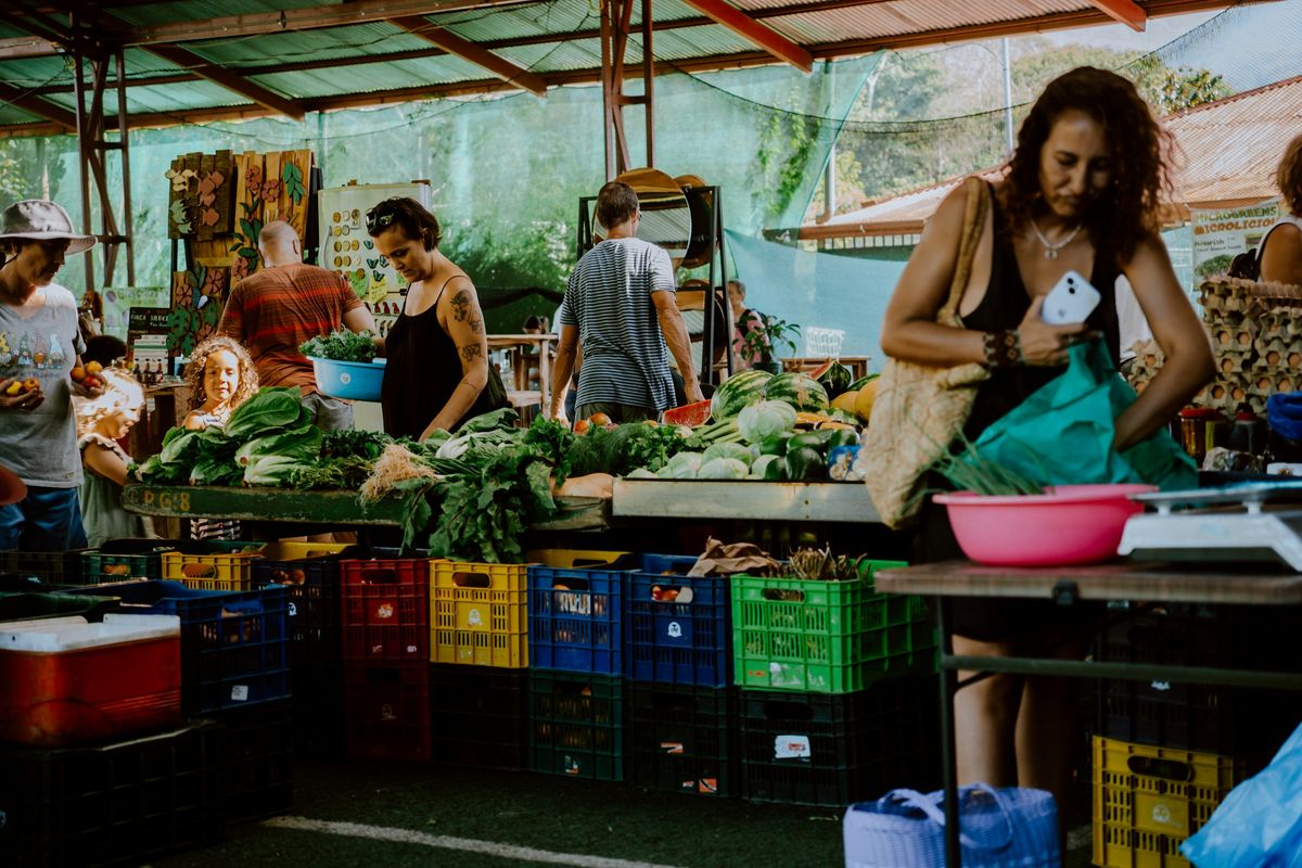 Shoppers at a farmers market stall piled with greens